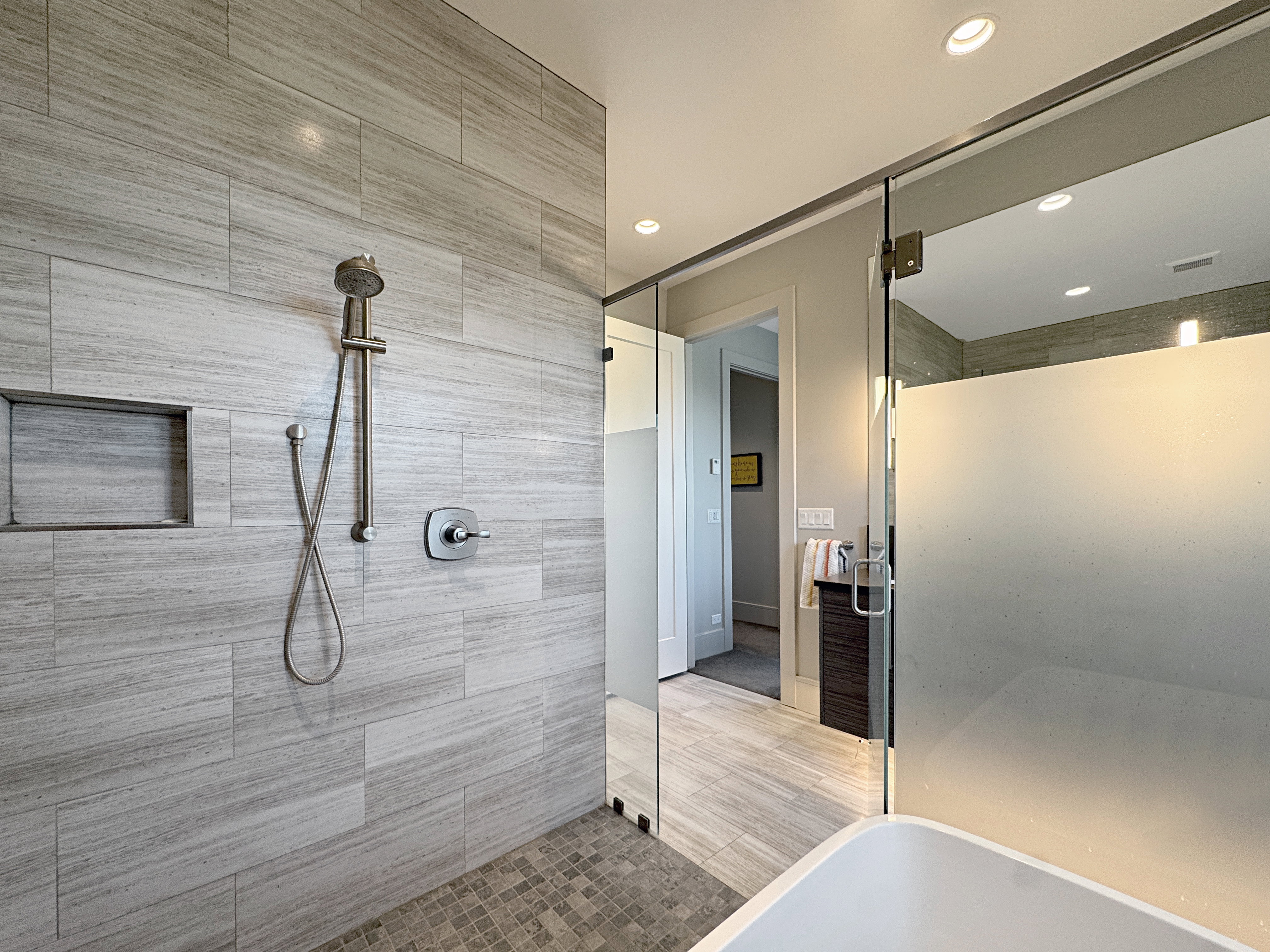 Walk-in shower featuring light grey tile walls, a built-in shower niche, and a handheld shower fixture