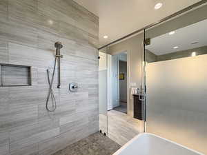 Walk-in shower featuring light grey tile walls, a built-in shower niche, and a handheld shower fixture