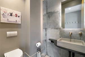 Bathroom featuring a wall-mounted toilet with flush plate, gray painted walls, and large format concrete-look wall tiling