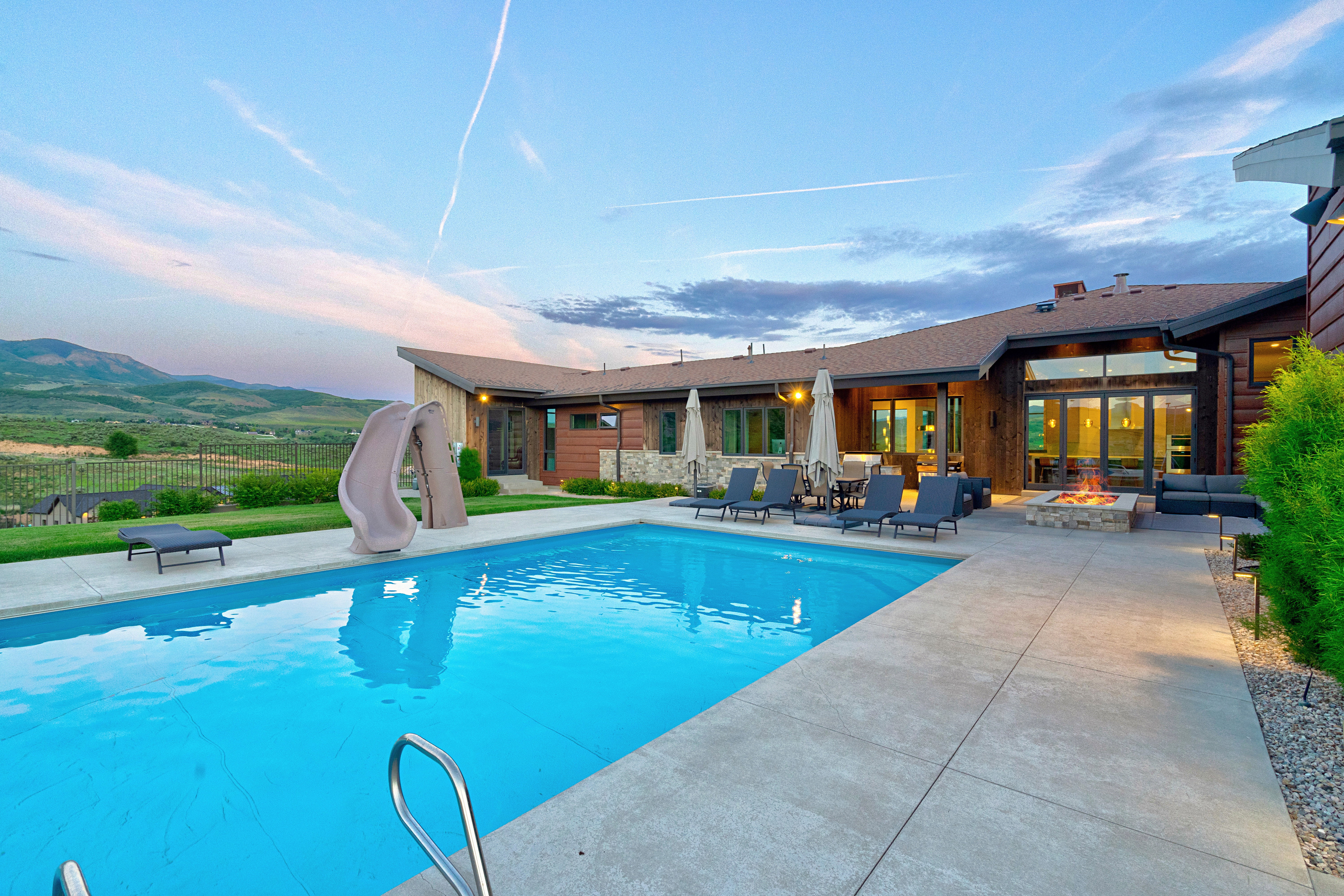 Expansive outdoor living area featuring a large swimming pool, concrete patio, built-in fire pit, and mountain scenery