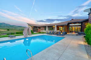Expansive outdoor living area featuring a large swimming pool, concrete patio, built-in fire pit, and mountain scenery