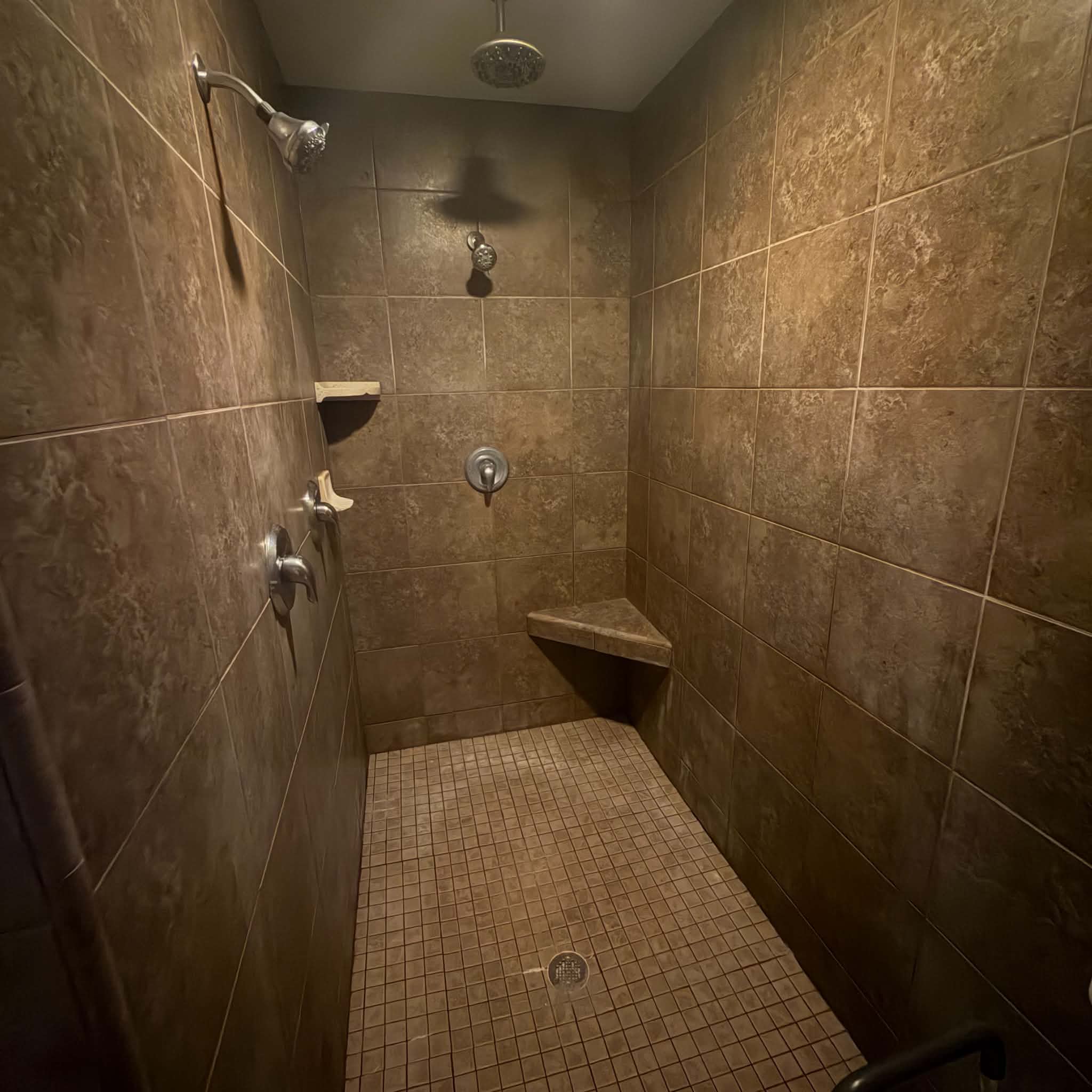 Tile-surround shower with a rainfall showerhead, handheld sprayer, and integrated corner bench