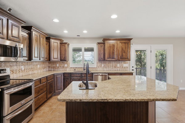 Kitchen featuring wood cabinetry, light-toned stone countertops, a stainless steel sink with a black faucet, and a patterned tile backsplash