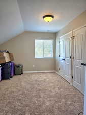 Carpeted room featuring a window with horizontal blinds, sloped ceiling, recessed lighting, and two bifold closet doors
