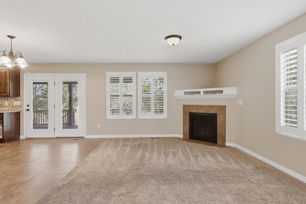 Living area featuring a textured carpet, a fireplace with a stone surround, and multiple windows with white plantation shutters