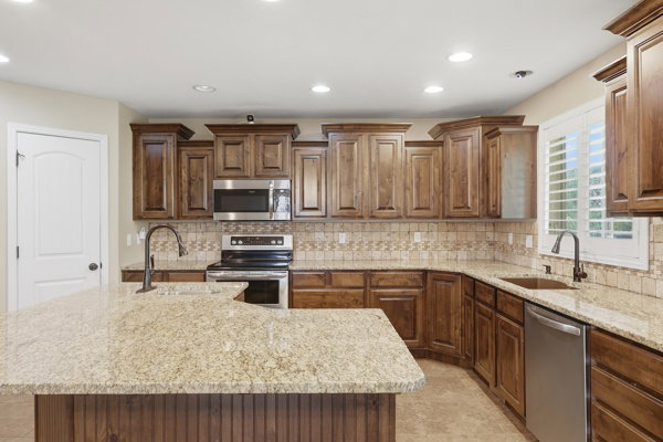 Kitchen featuring granite countertops, wood cabinetry, stainless steel appliances, and a tiled backsplash