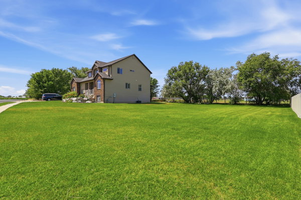 Expansive green lawn with mature trees and a residential property featuring brick and siding exterior, multiple gables, and a curved driveway