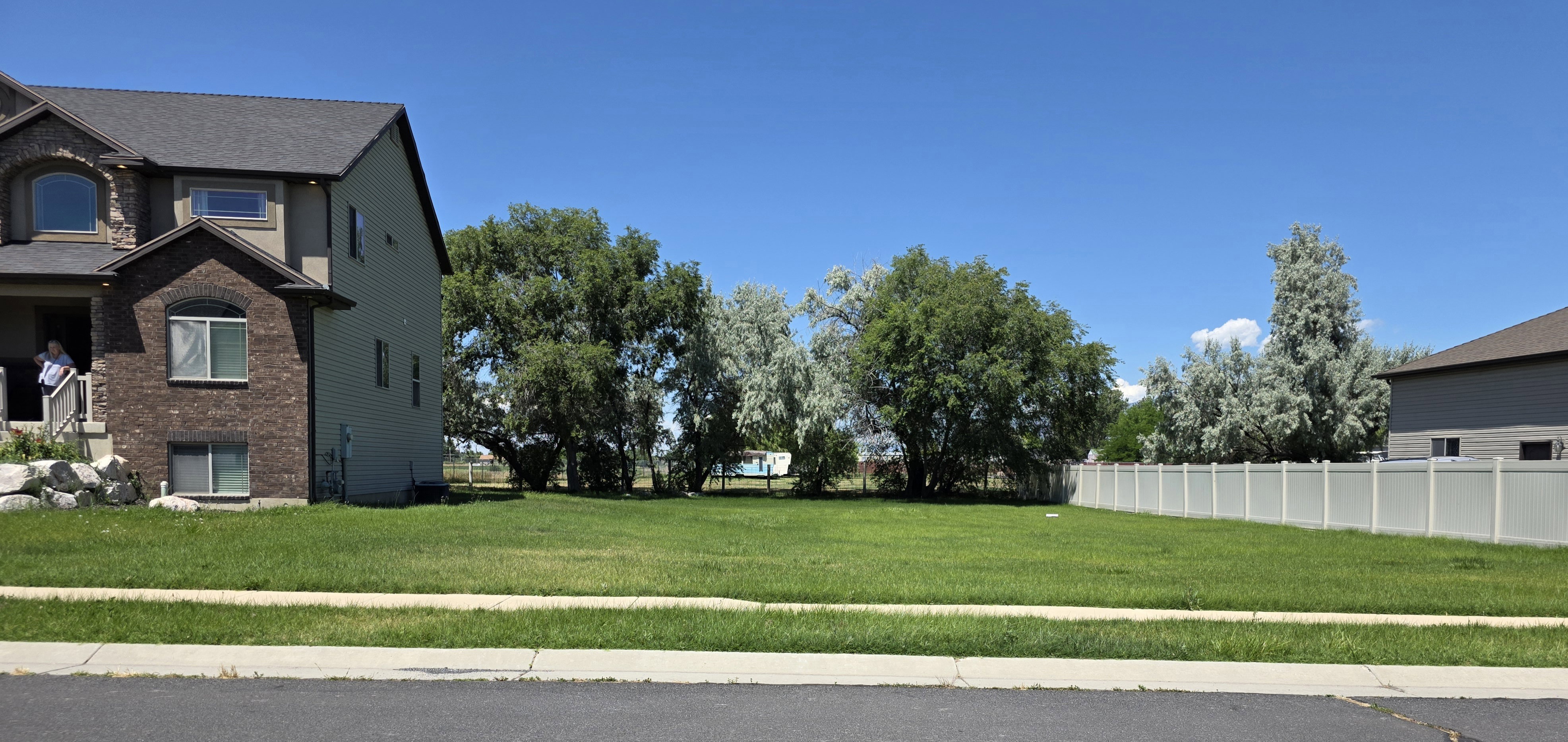 Expansive green lot featuring mature trees and a white privacy fence