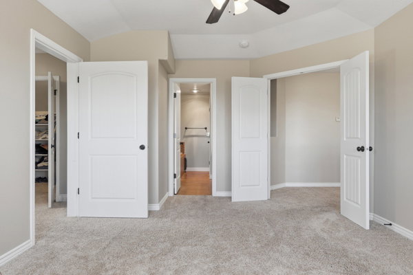 Plush carpeted room featuring white paneled doors with black hardware, a ceiling fan with integrated lighting, and neutral wall tones