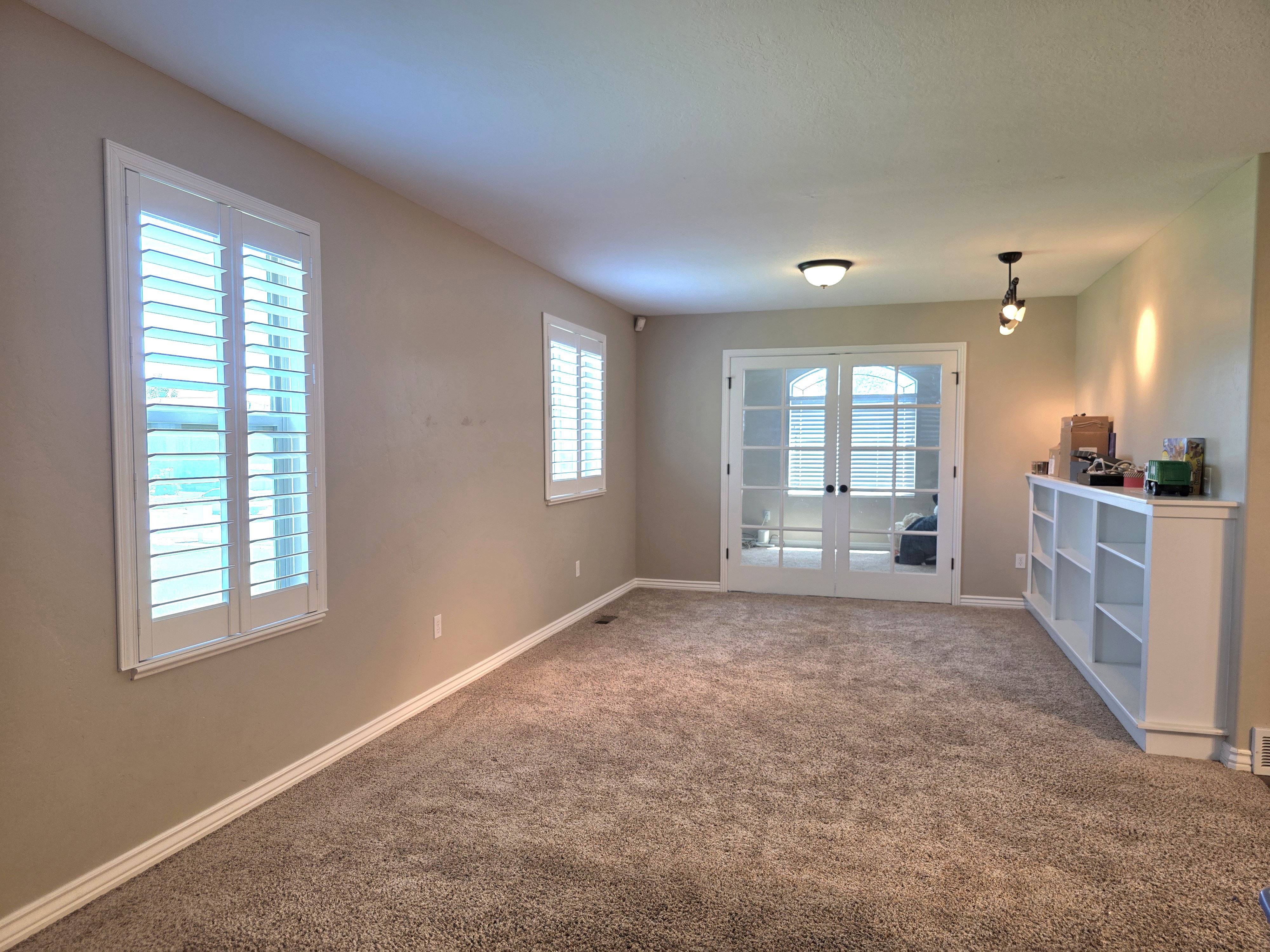 Carpeted interior space featuring white plantation shutters, neutral wall paint, and white baseboards