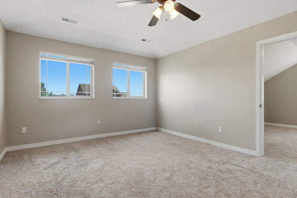 Neutral-toned room featuring a ceiling fan with integrated lighting, two windows, and light-colored carpet flooring