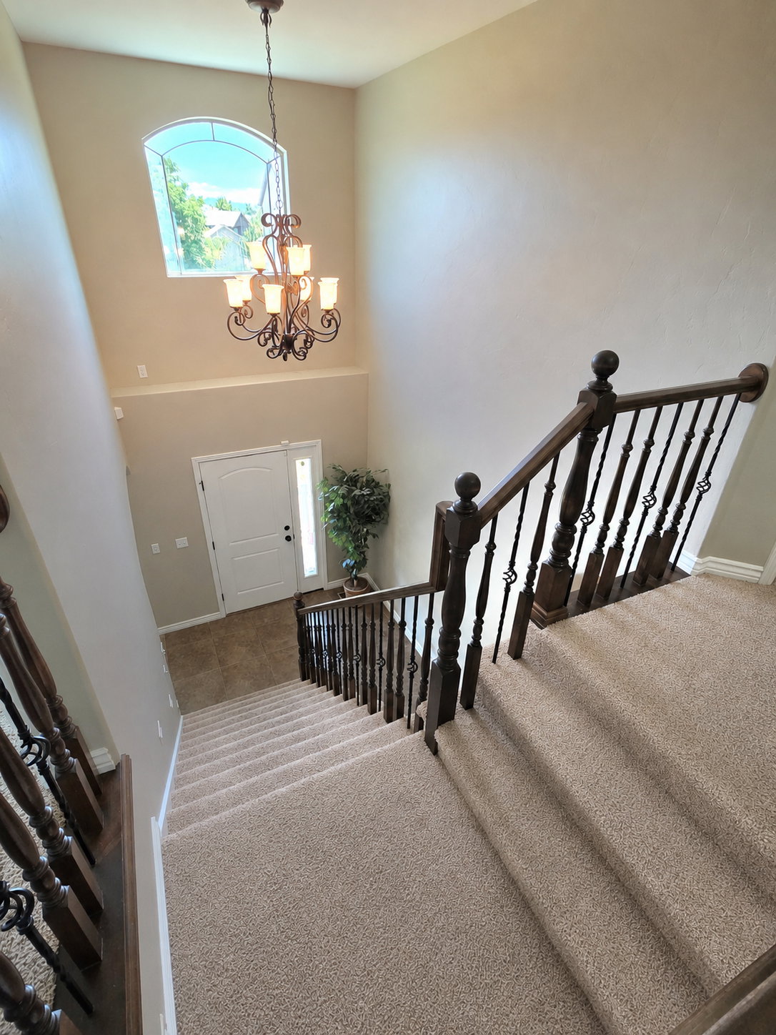 Two-story entryway featuring a grand chandelier, arched window, and dual entry doors with a sidelight