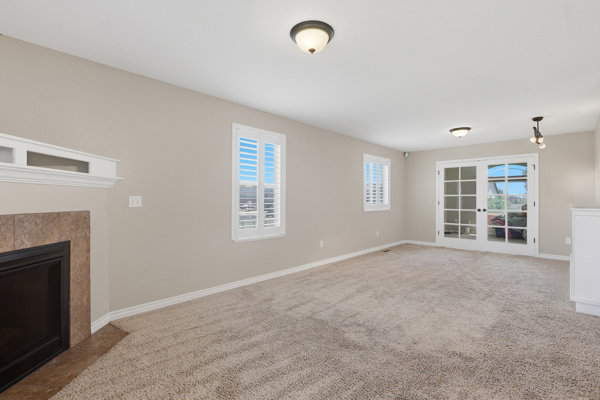 Carpeted living area featuring a fireplace with a tile surround and mantel, two windows with white plantation shutters, and double glass-paned doors