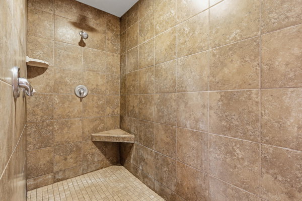 Shower enclosure featuring neutral-toned wall tiles, a mosaic tile floor, and a built-in corner bench