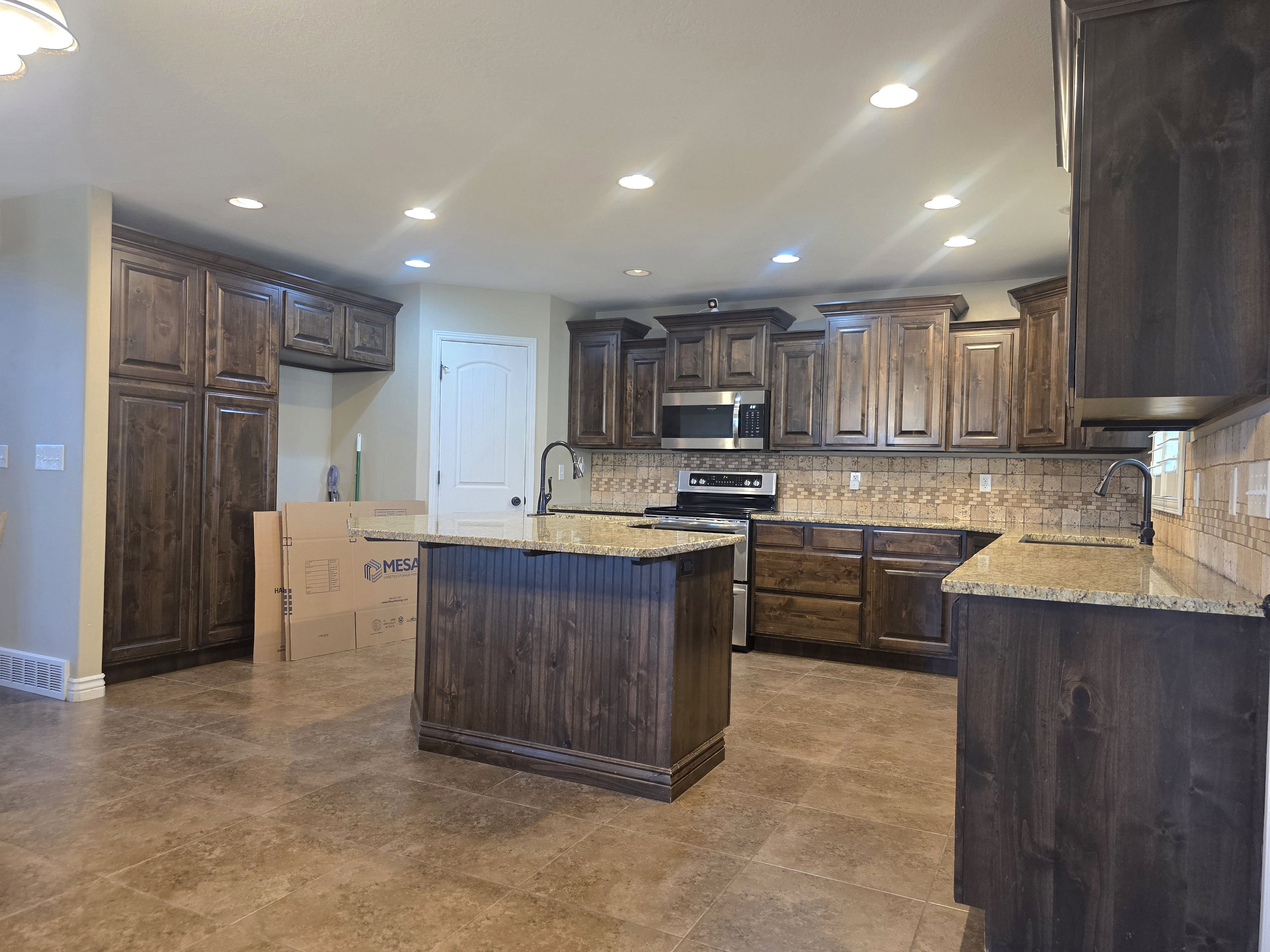 Kitchen featuring dark wood-finish cabinetry, granite countertops, stainless steel appliances, a center island with beadboard paneling, and ceramic tile flooring