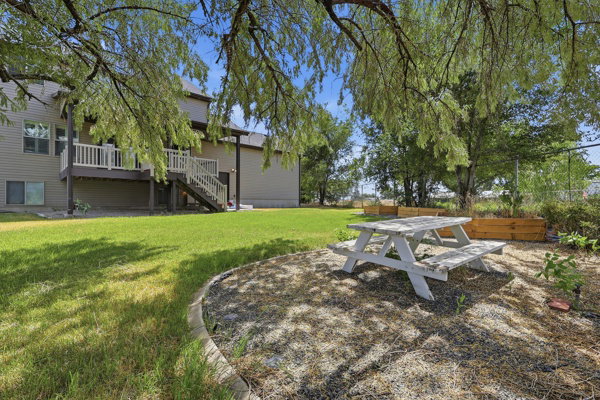 Expansive backyard featuring a manicured lawn, a two-story exterior with siding, a raised deck with white railings, and a gravel patio area with mature trees