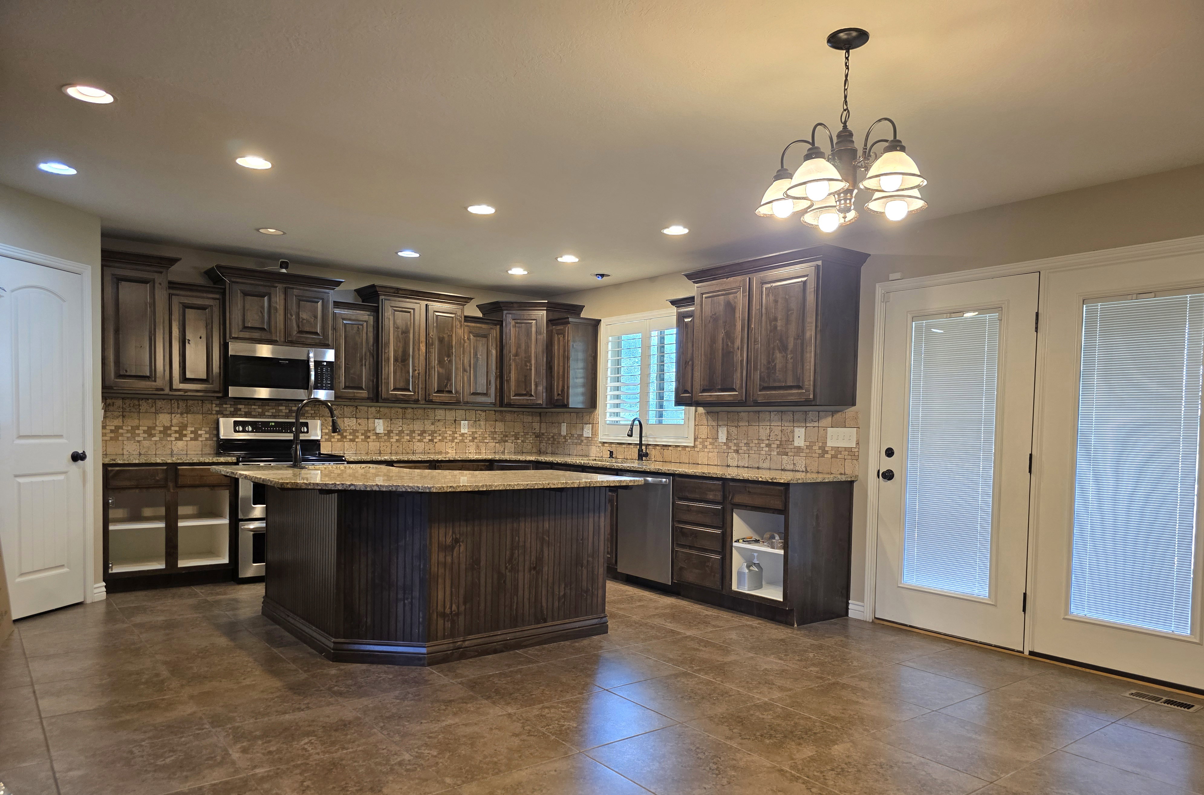 Kitchen featuring a large island with integrated sink, dark wood-finish cabinetry, speckled countertops, and a tiled backsplash