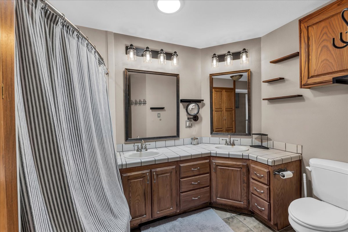 Bathroom featuring a dual vanity with wood cabinetry, tile countertops, two undermount sinks, jetted tub