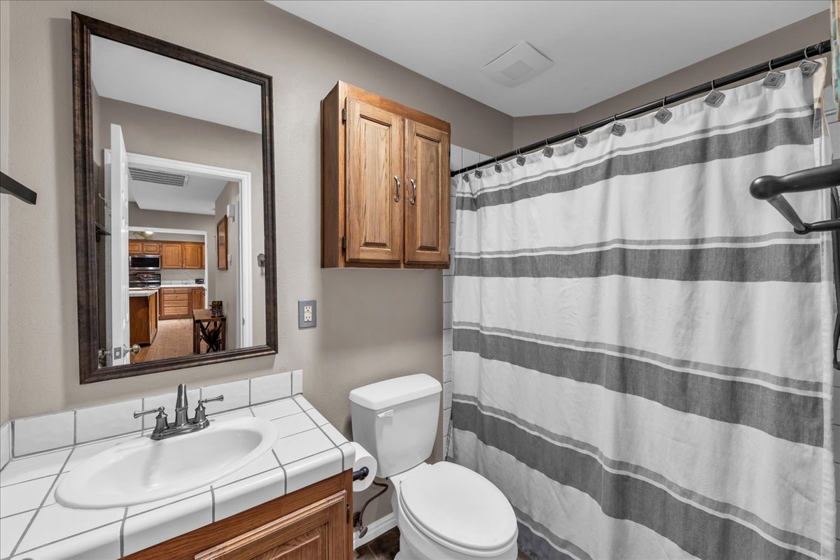 Bathroom featuring a ceramic tile countertop with integrated sink, wood-finish vanity, and overhead wood-finish cabinetry
