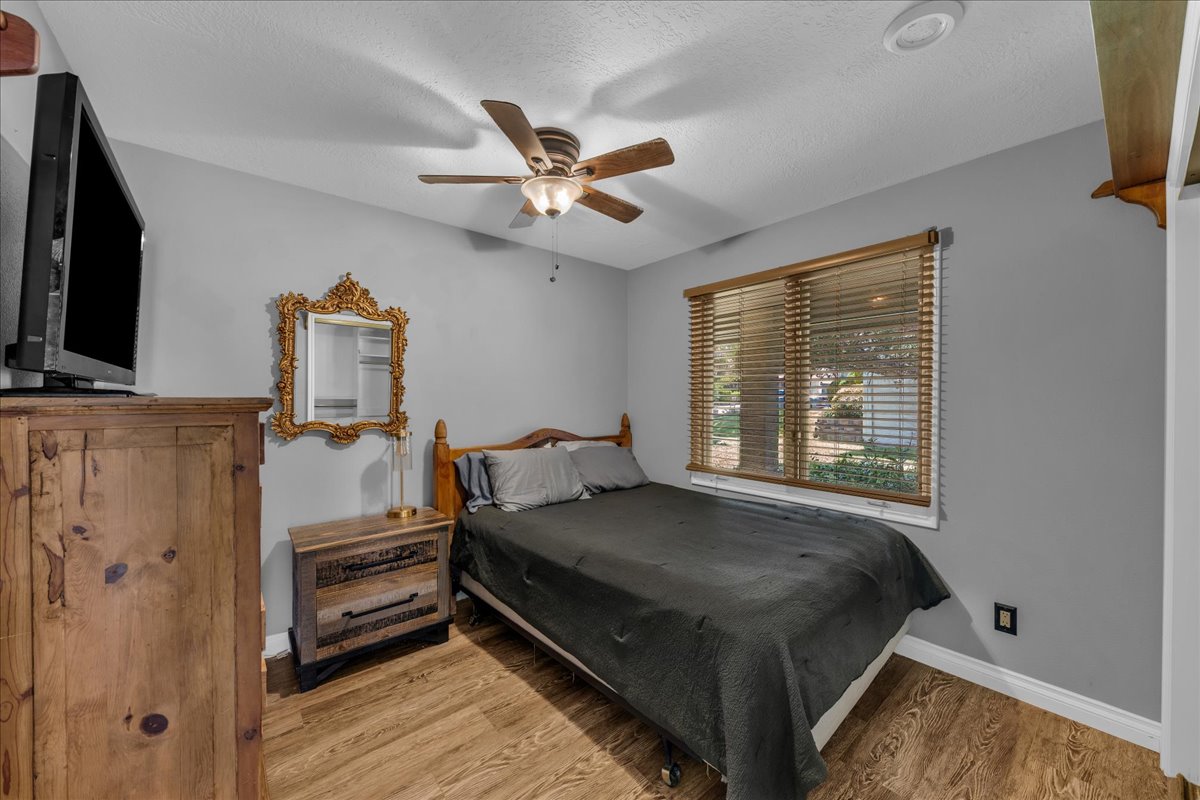 Bedroom featuring wood-finish flooring, a window with wood blinds, and ceiling fan