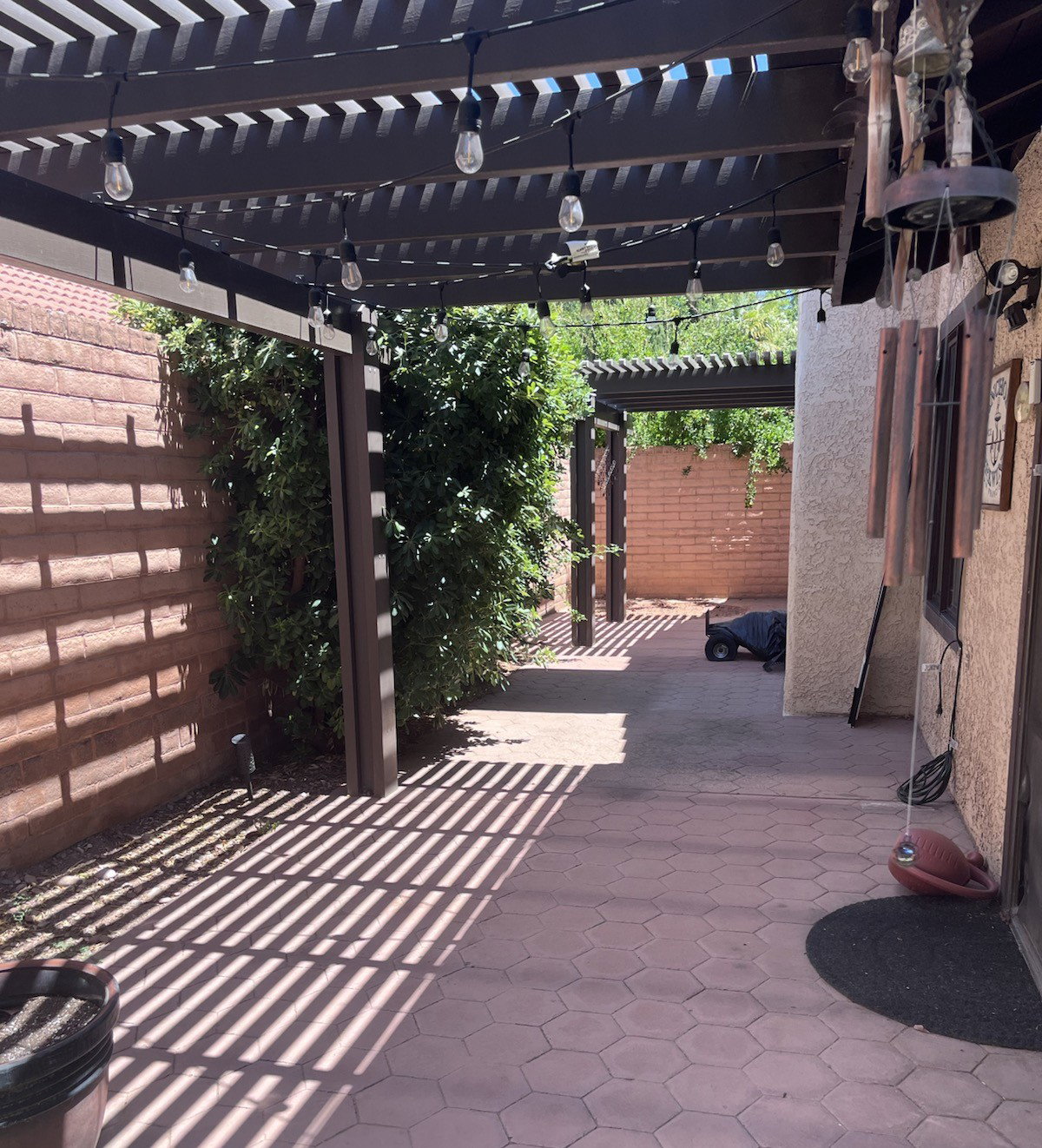 Expansive patio featuring hexagonal pavers, a pergola with string lighting, and mature perimeter landscaping