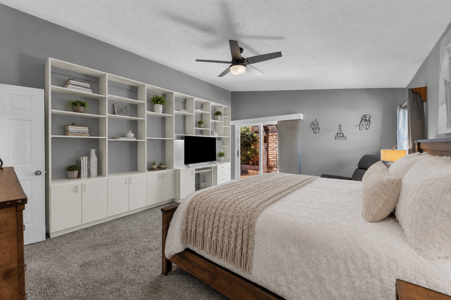 Expansive bedroom featuring a full-wall built-in shelving unit with lower cabinetry, a ceiling fan, and newer carpet.