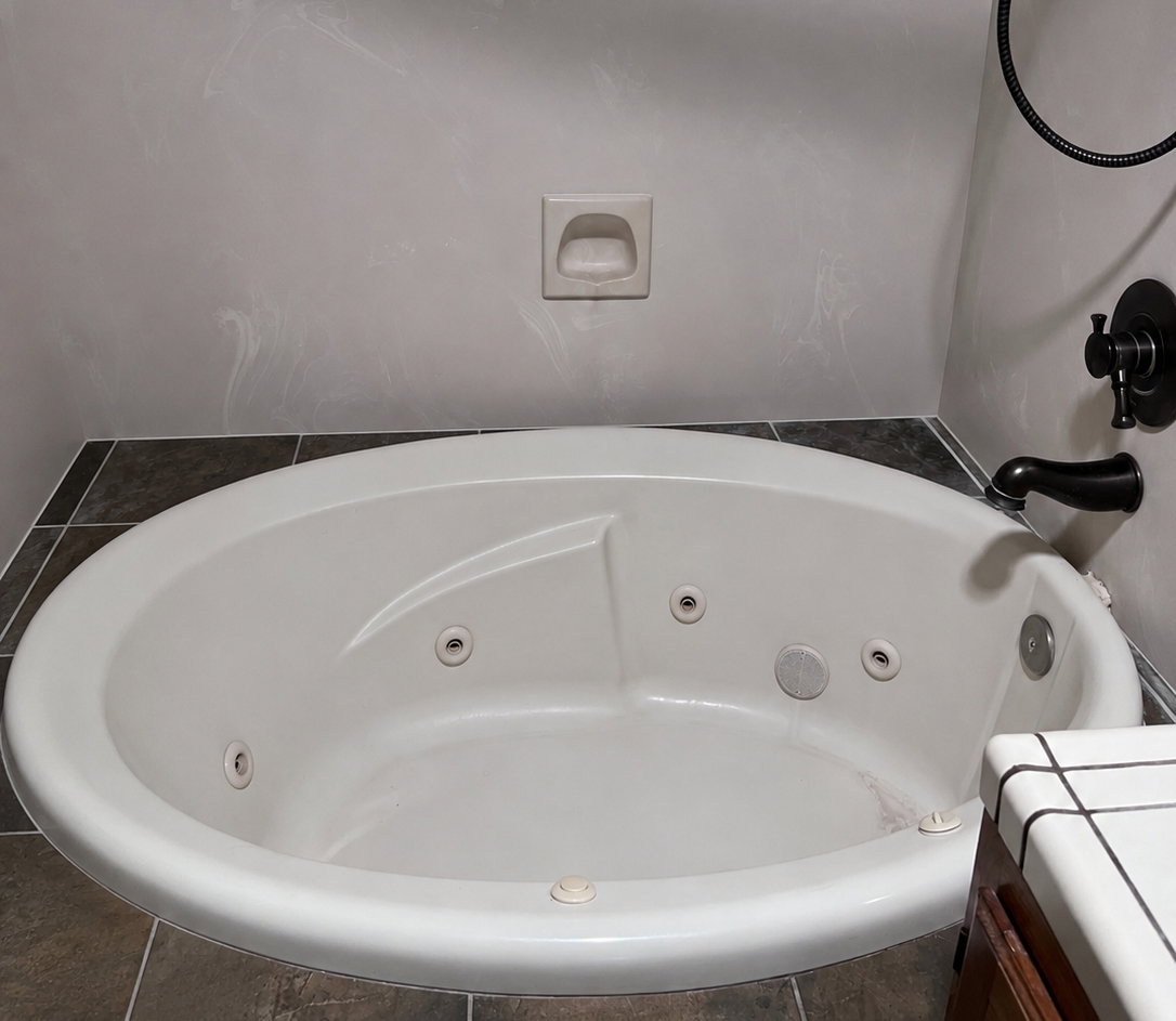 Oval jetted bathtub set into tile, featuring a dark bronze faucet and a built-in soap holder