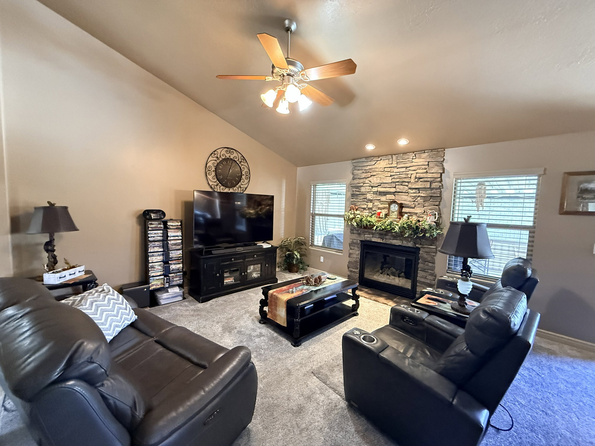 Living room featuring a stone-faced fireplace with a black insert, vaulted ceiling, and recessed lighting
