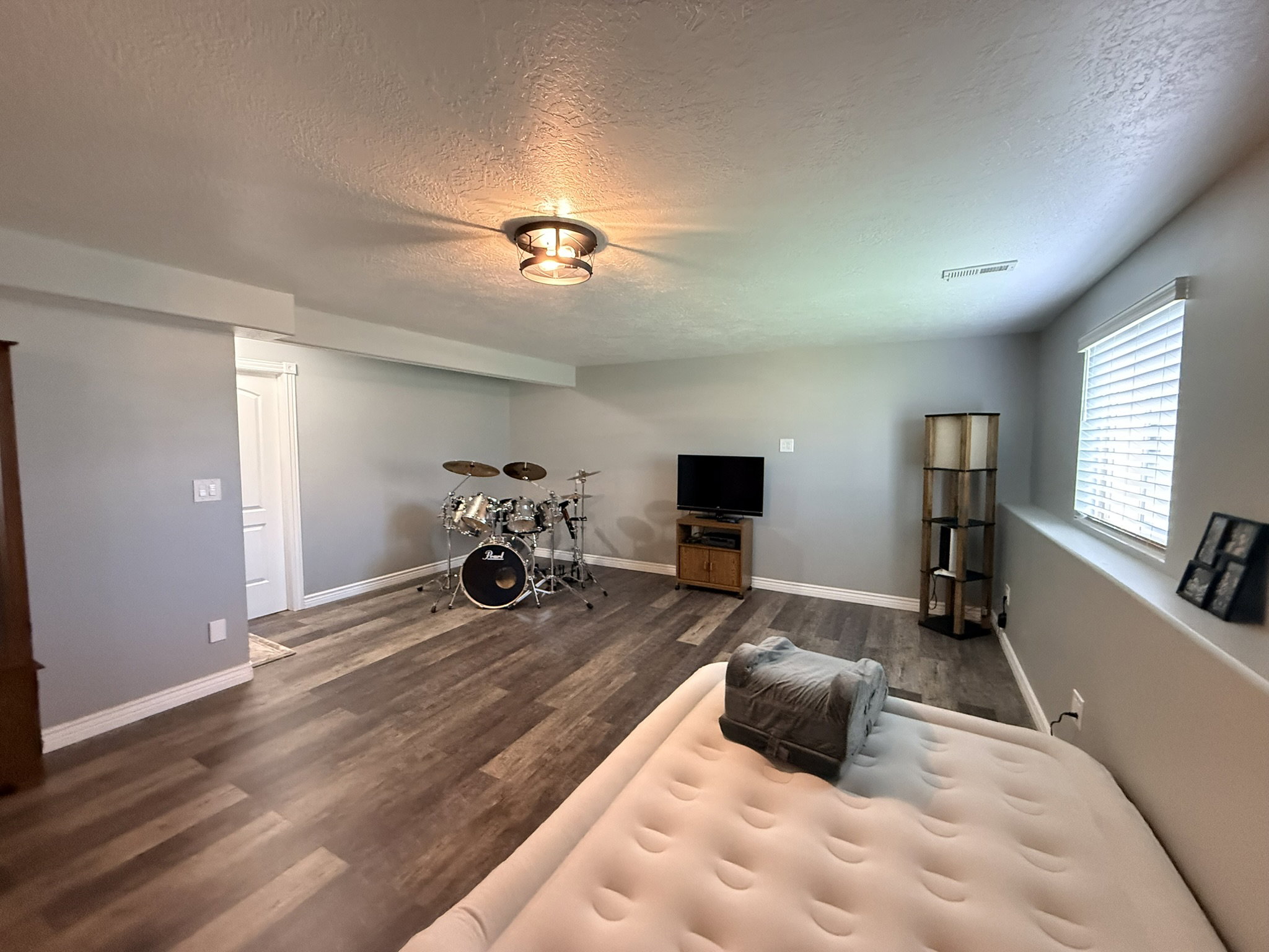 Spacious room featuring wood-finish flooring, light gray walls, and a recessed window with blinds