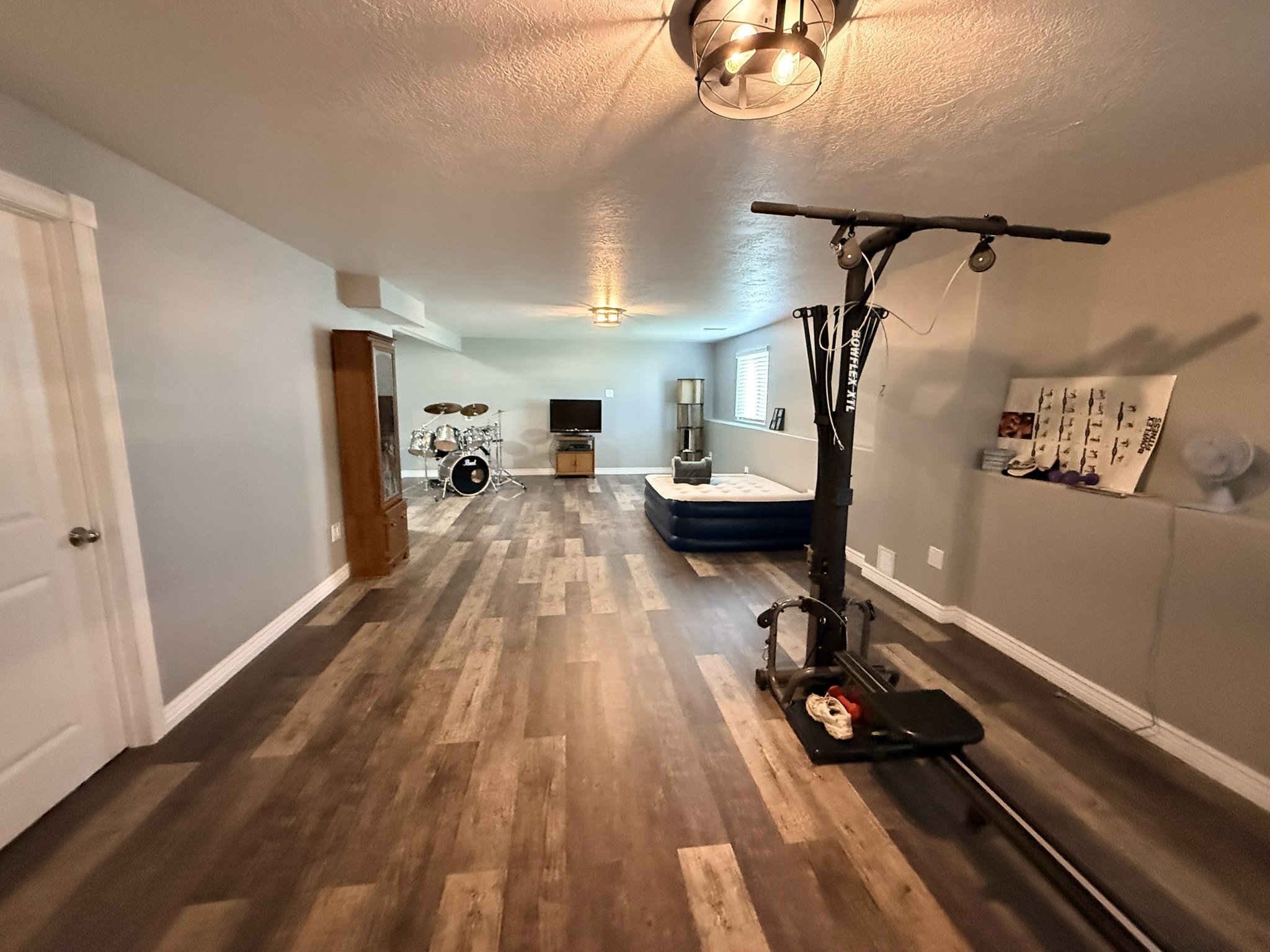 Spacious lower-level room featuring wood-finish flooring, light gray walls, and white trim