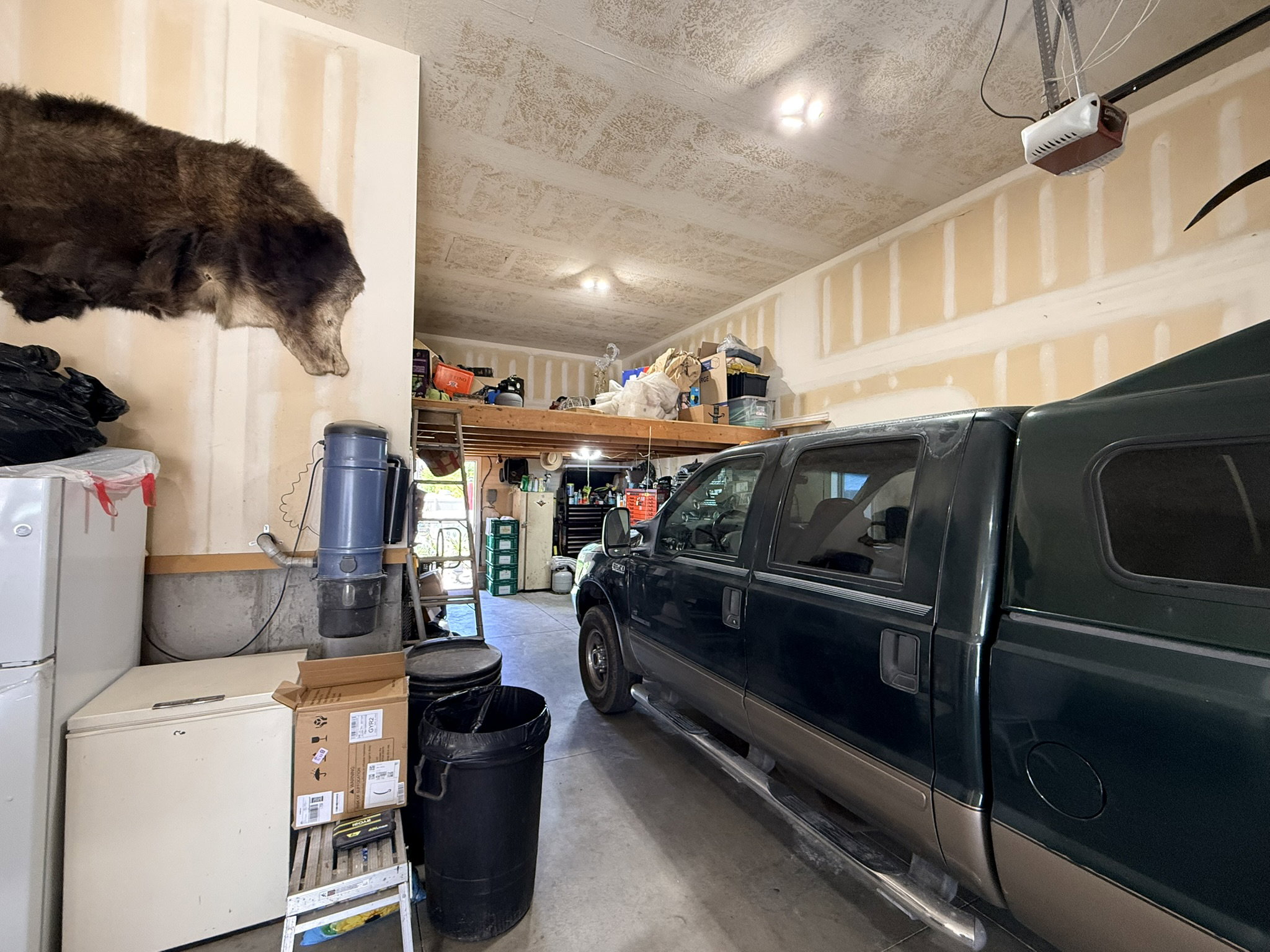 Spacious garage featuring a high ceiling, exposed wall studs, and overhead storage loft