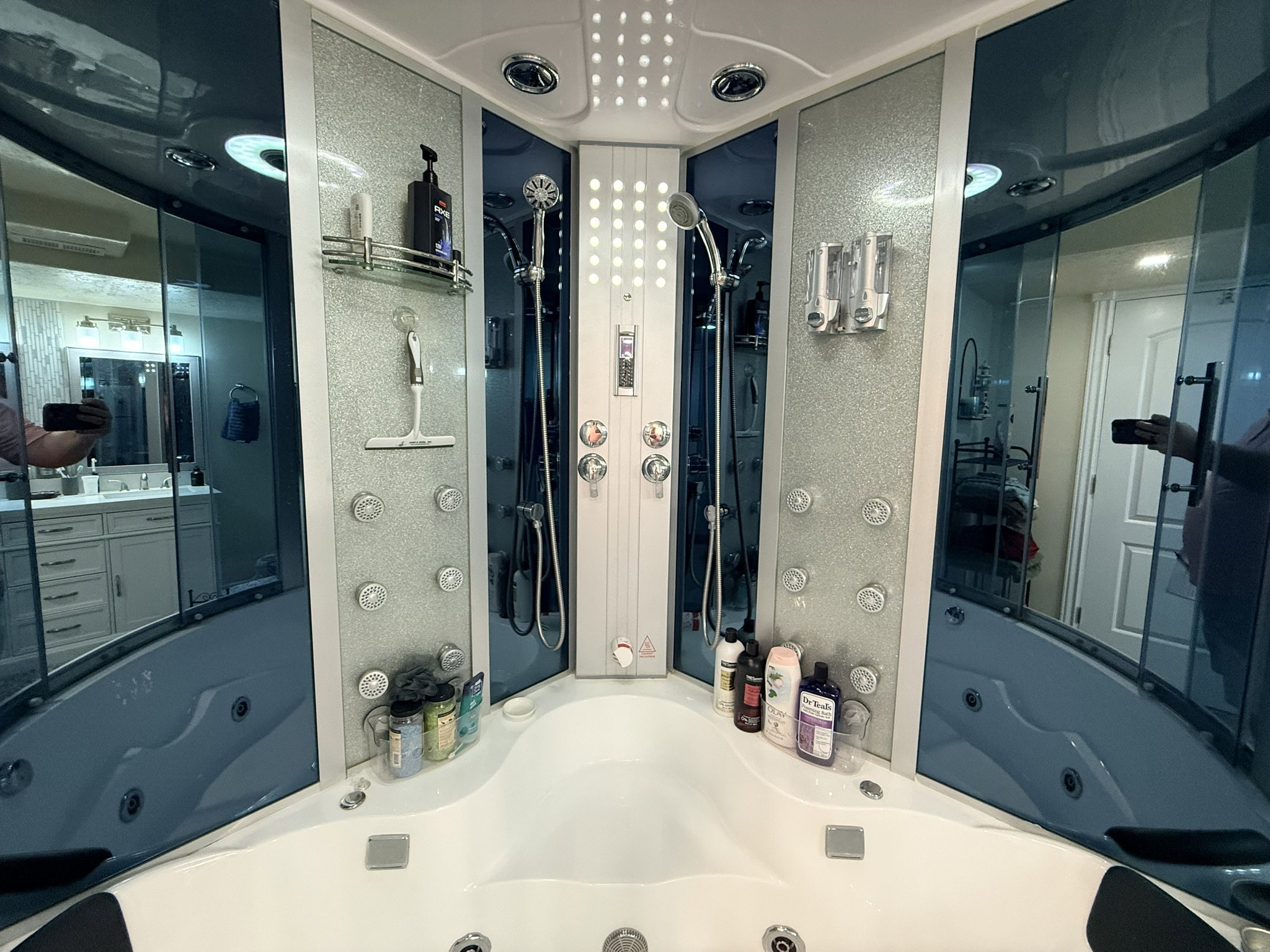 Integrated shower and jetted tub system featuring multiple body sprayers, a handheld shower fixture, and overhead lighting