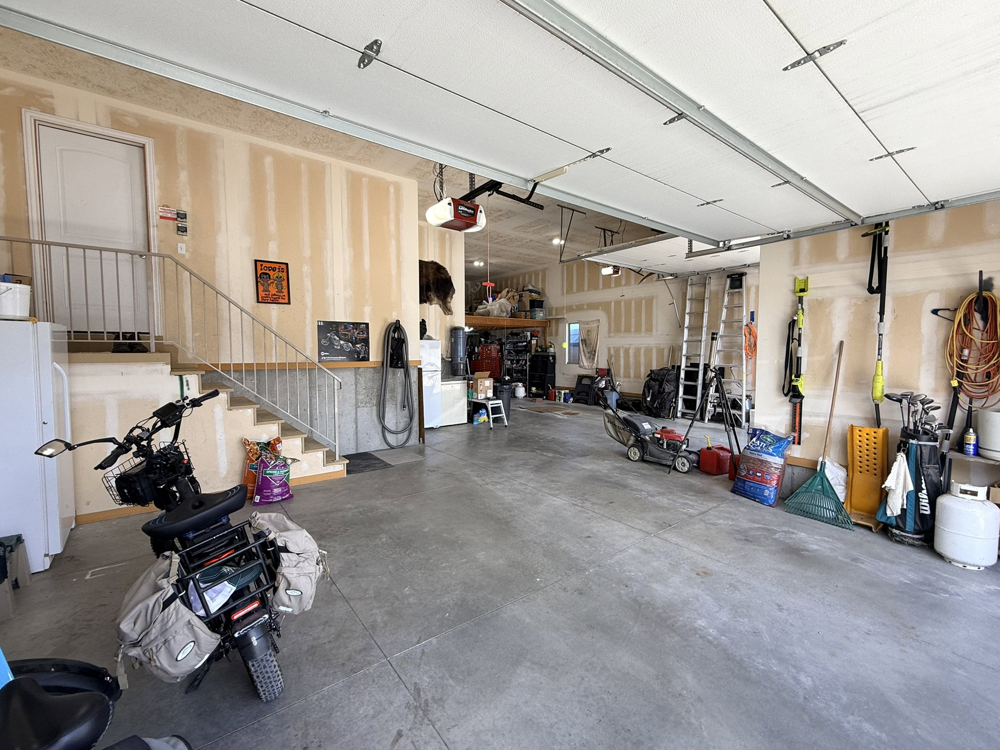 Spacious garage featuring a concrete floor, overhead garage doors, an interior staircase with metal railing, and an interior door