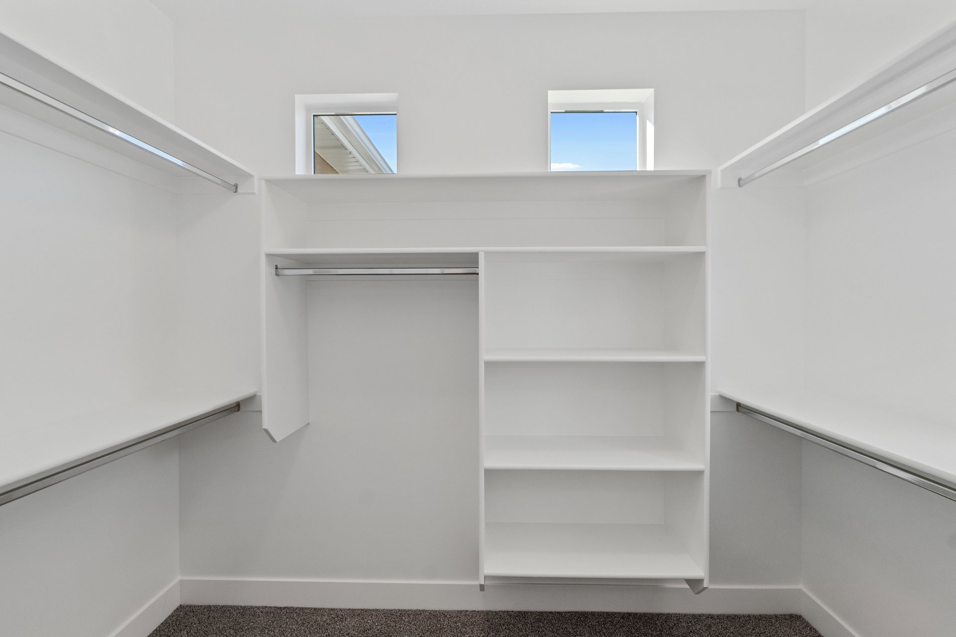 Walk-in closet featuring built-in shelving, multiple hanging rods, and twin transom windows