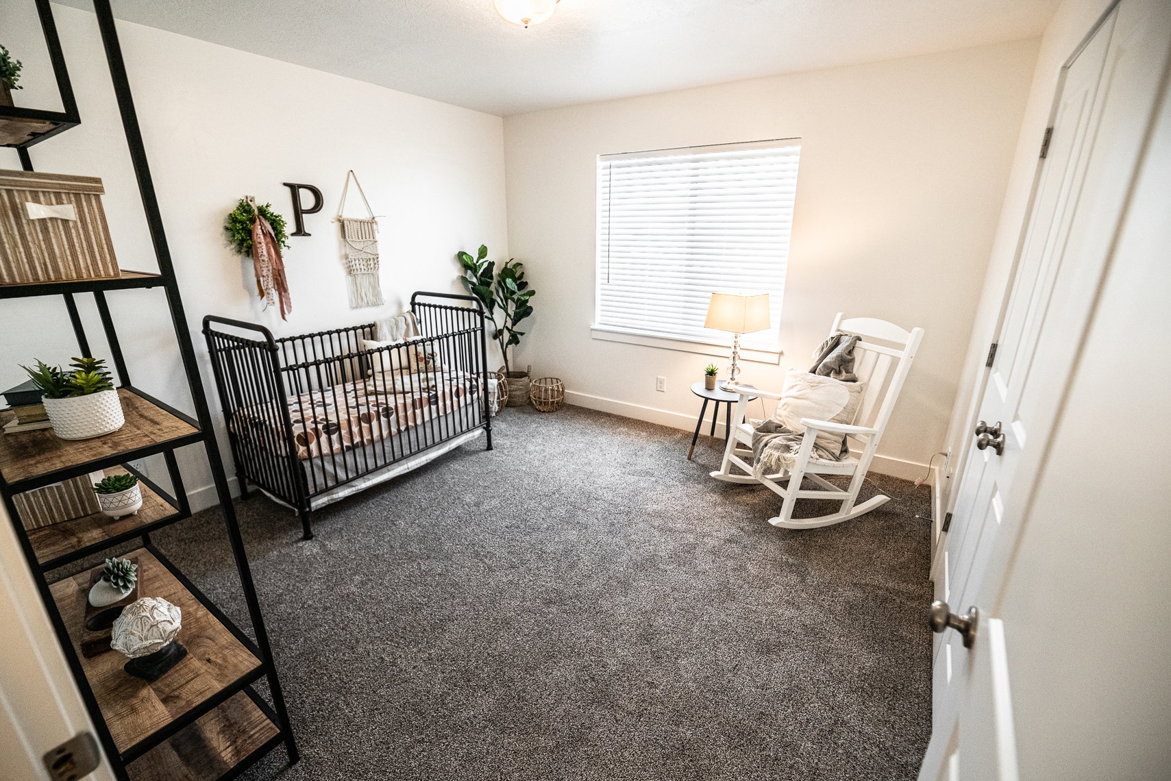 Carpeted room featuring a window with horizontal blinds, a white paneled door with dark hardware, and a ceiling-mounted light fixture