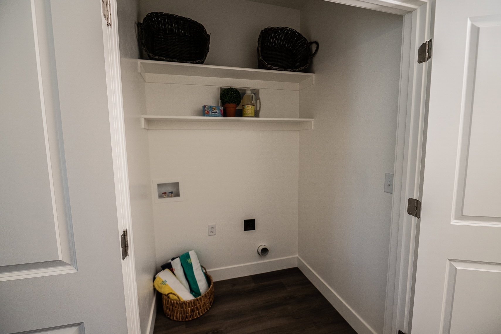 Dedicated laundry closet featuring a dark wood-finish floor, white walls, and two integrated shelving units
