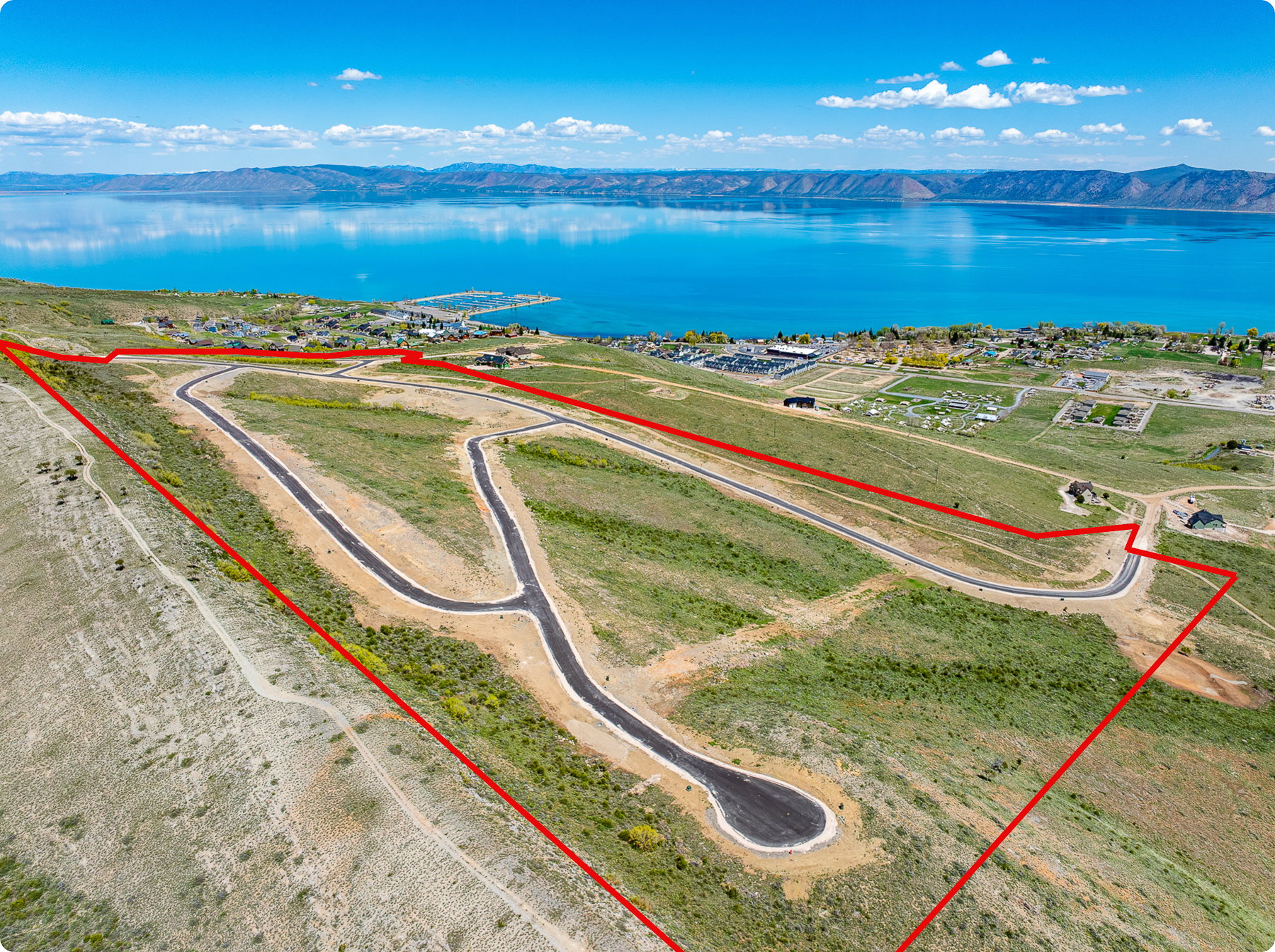 Expansive land parcel featuring paved roads, cul-de-sac, and clear boundaries, with a prominent lake and distant mountains in the background