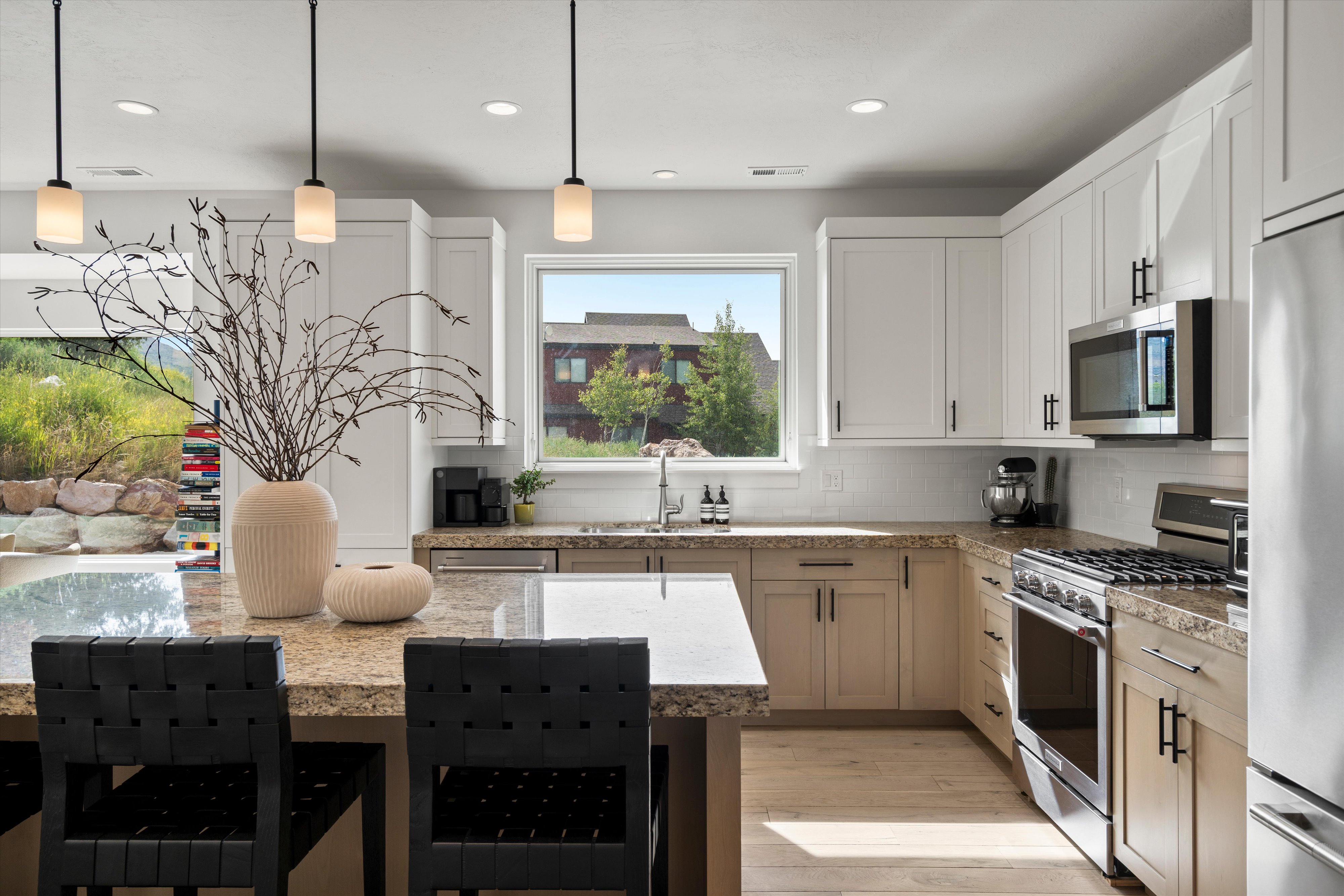 Spacious kitchen featuring a large island with a granite countertop, light wood-finish flooring, white upper cabinetry, and stainless steel appliances.