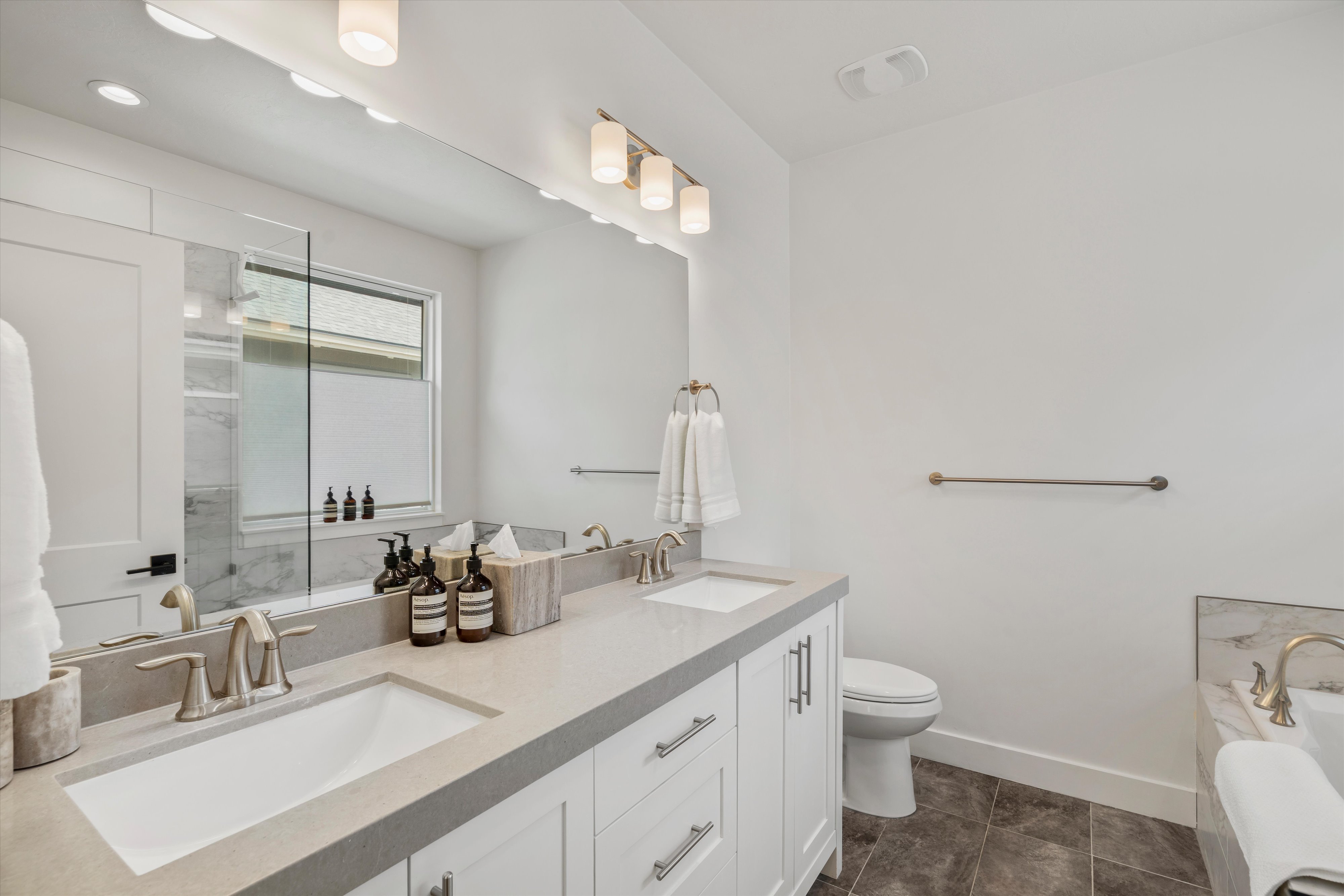 Bathroom featuring a double vanity with light gray countertops and undermount sinks, white cabinetry with brushed nickel hardware, and a large mirror with integrated lighting