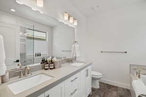 Bathroom featuring a double vanity with light gray countertops and undermount sinks, white cabinetry with brushed nickel hardware, and a large mirror with integrated lighting