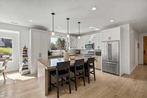 Kitchen featuring light wood-finish flooring, white cabinetry, stainless steel appliances, and a granite countertop island with seating.