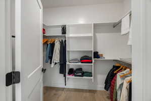 Primary suite walk-in closet system featuring multiple shelves, hanging rods, and light wood-finish flooring
