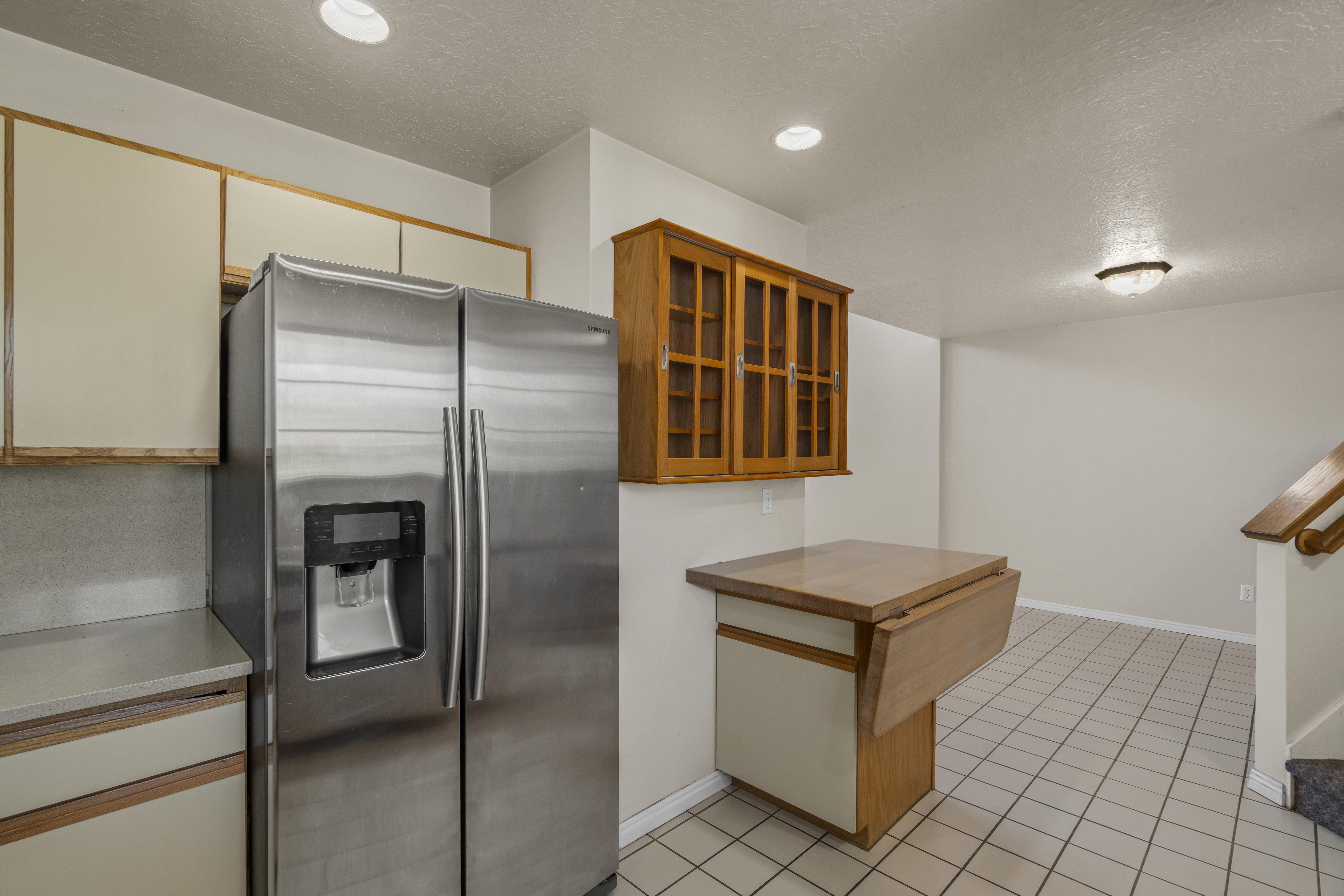Kitchen area featuring a stainless steel side-by-side refrigerator, cream-colored upper and lower cabinetry, and a wood-finish drop-leaf counter