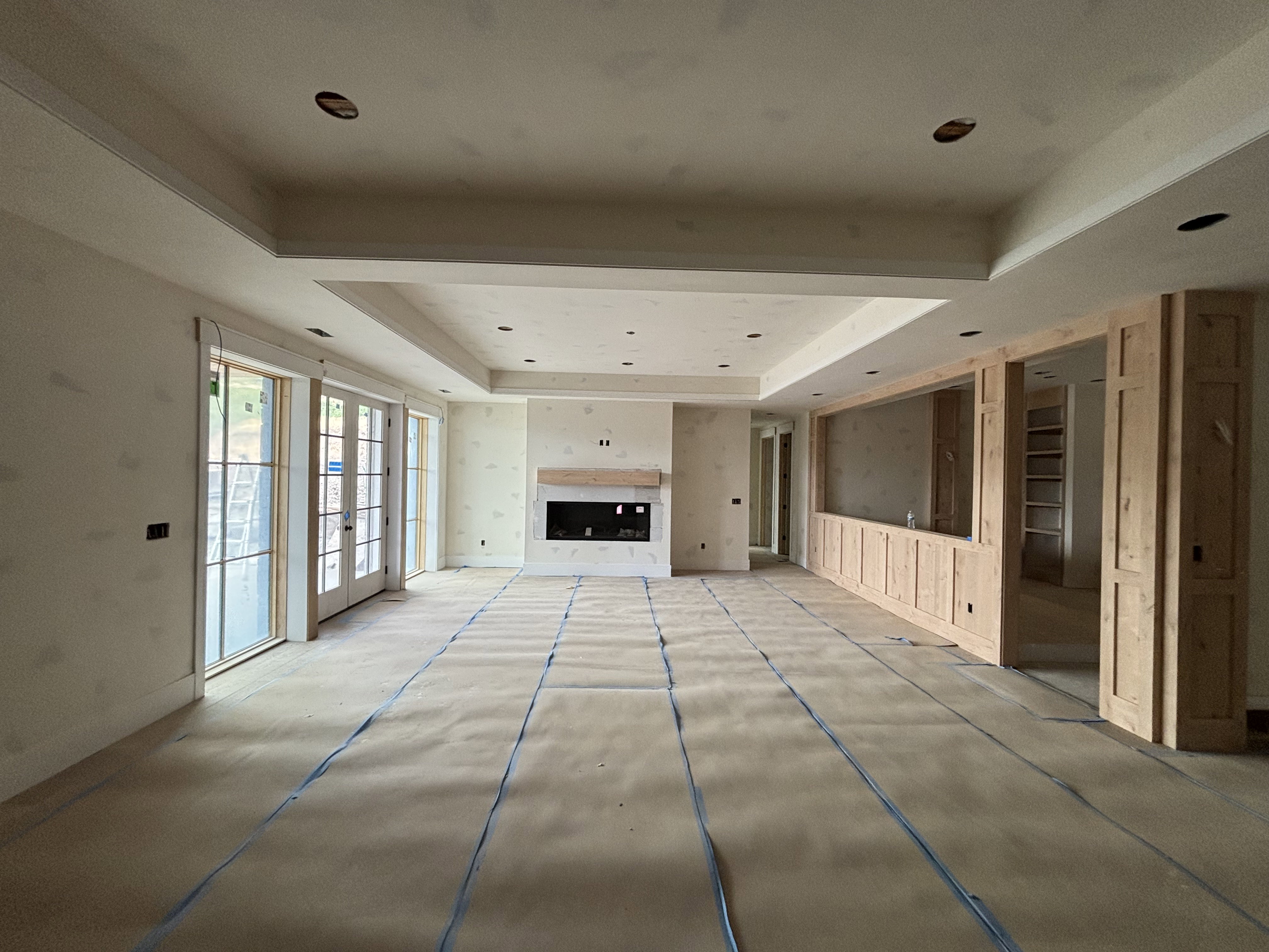 Spacious basement living space featuring a fireplace, tray ceiling, and French doors