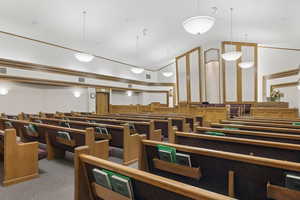 Spacious interior featuring multiple rows of built-in wooden seating with upholstered backs, integrated lighting, recessed wall panels with wood trim, and a high vaulted ceiling with pendant and wall sconce lighting.