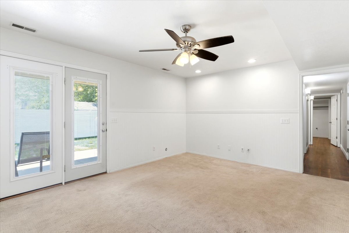 Carpeted room featuring dual glass-paned doors, beadboard wainscoting, a ceiling fan with light fixture, recessed lighting, and a wood-finish flooring hallway