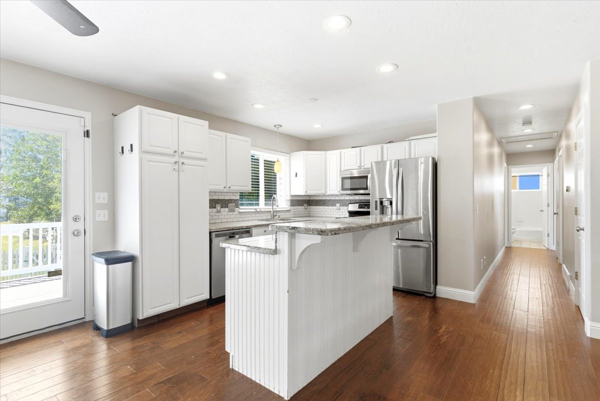 Bright kitchen featuring white cabinetry, stainless steel appliances, a center island with a granite countertop, and wood-finish flooring