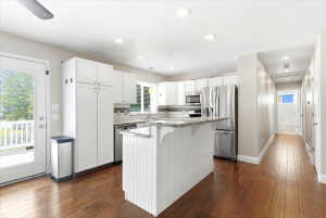 Bright kitchen featuring white cabinetry, stainless steel appliances, a center island with a granite countertop, and wood-finish flooring