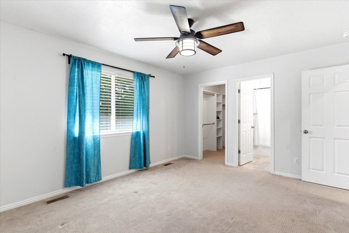 Light-colored carpeting throughout, featuring a window with horizontal blinds and teal drapery