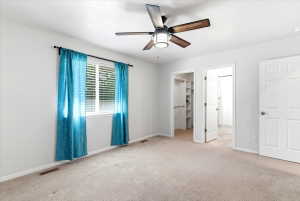 Light-colored carpeting throughout, featuring a window with horizontal blinds and teal drapery
